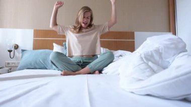 Genç bir kadın uyanıyor ve otel odasında yatakta dans ediyor.