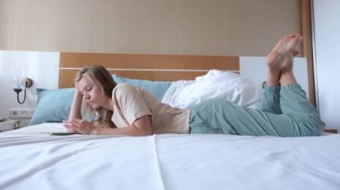 Uyandıktan sonra otel yatağında akıllı telefon kullanan genç bir kadın.