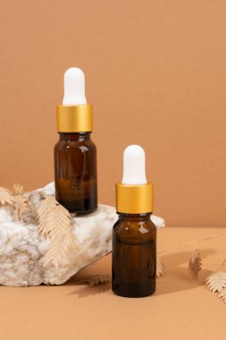 Kahverengi arka planda kehribar cam damlası şişesi, taşlar ve doğal kozmetik bileşimi.
