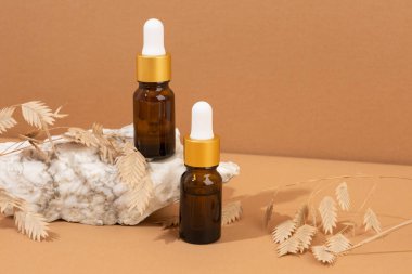 Kahverengi arka planda kehribar cam damlası şişesi, taşlar ve doğal kozmetik bileşimi.