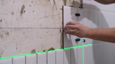 Elleri duvara seramik seramik seramik seramik seramik seramik döşeme yapıyor. Elektronik lazer seviyesi kullanılıyor.