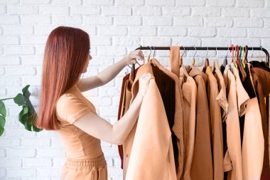 2024 yılının rengi: Şeftali tüyü. Bej ceketli güzel bir kadın askılığın önünde duruyor ve elbise giymeyi seçiyor. Gardırop seçimi, stilist, alışveriş. Giysi Tasarımı
