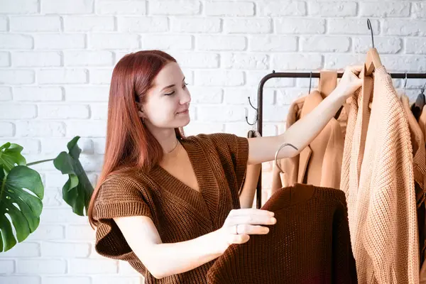 2024年的颜色 Peach Fuzz 穿着米色外套的年轻漂亮的女人站在衣架前挑选服装 选择衣橱 造型师 购物者 服装设计 免版税图库照片
