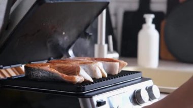 Kadın mutfakta somon bifteği pişiriyor.