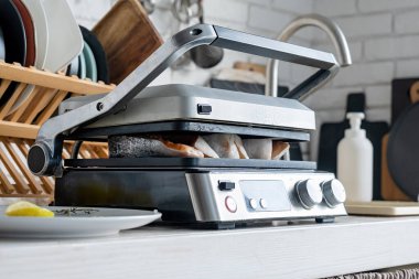 Mutfak masasında balık ve et ızgarası. Mutfaktaki elektrikli ızgarada pişmeye hazır taze alabalık bifteği.