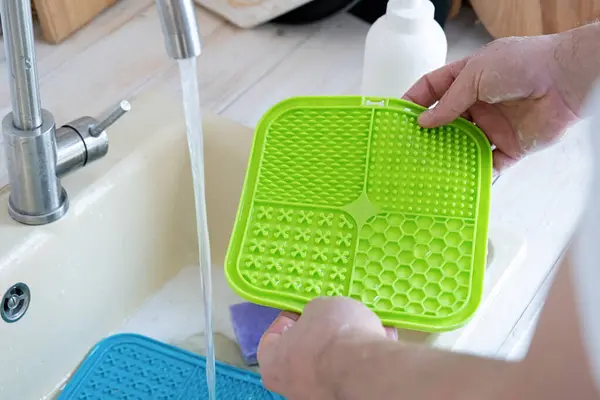 hands washing pet lick mat in kitchen sink . snack mat, licking mat for cats and dogs