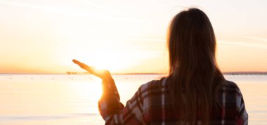 Kumsalda gün batımı siluetiyle güneşi tutan eller.