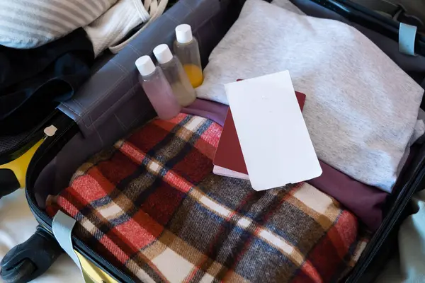 happy woman preparing for holidays, packing suitcase on bed, blank boarding pass
