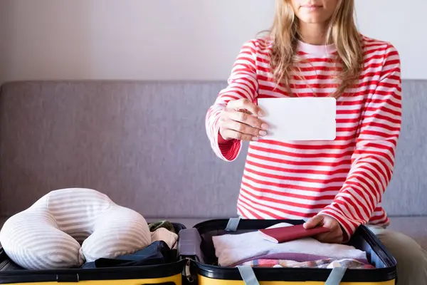 happy woman preparing for holidays, packing suitcase on bed, woman holding a blank boarding pass