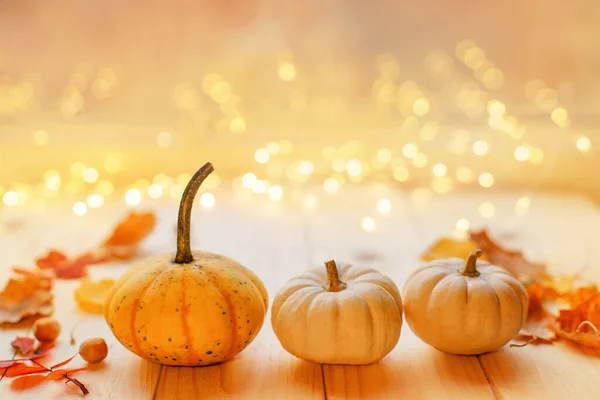 Tahta yüzeyde üç balkabağı ve renkli yapraklar var ve ışıklar bokeh. Samimi düşüş havası. Şükran Günü. 