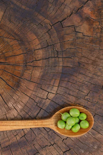 Wood spoon with green peas on wood background