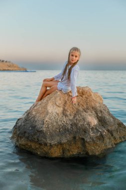 Gün batımında deniz kenarında taş üstünde bir kız. Sakin, sakin..