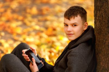 A teenage boy sits on a bench with his arms stretched along the backrest, eyes closed, fully immersed in the music playing in his headphones.  clipart