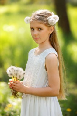 Güneşli yeşil bir ormanda oturan, elinde bir buket kabarık karahindiba tutan ve beyaz dantelli elbise giyen uzun sarı saçlı çekici bir kızın portresi.. 