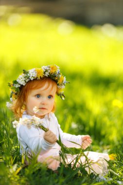 Şirin küçük kız açık havada güzel bir bahar çelengi giyiyor, mesaj için yer var. Kızıl saçlı bebek doğada vakit geçiriyor. 