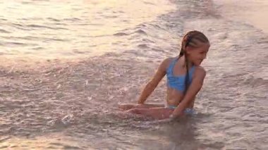 Bir sürü örgüsü olan 9 yaşındaki bir kız gün batımında deniz suyunda oturur. Biri onu kameranın dışından su sıçratıyor ve o da mutlu bir şekilde iki eliyle geri sıçrıyor, neşeli bir su savaşına yakalanıyor..