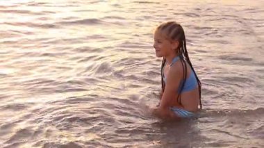 9 yaşında bir kız gün batımında deniz suyunda oturur. Bir an için utangaç bir şekilde kameraya bakıyor, sonra kendi aktivitelerine geri dönüyor, doğal ve samimi bir anı yakalıyor..
