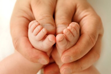 Bir babanın elleri, parmakları çerçevenin ortasında olan bir bebek bacağını nazikçe kucaklıyor..