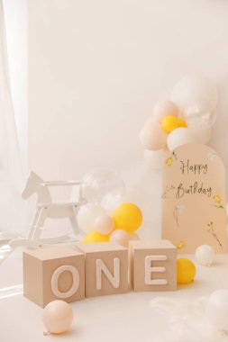 Tarafsız ve sarı temalı ilk doğum günü partisi dekoratif engeller 1, sarı elbiseli şirin tavşan figürü, balonlar, beyaz sallanan at ve parlak bir stüdyoda yumuşak beyaz bir halı.