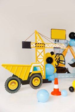 İnşaat temalı çocukların doğum günü partisi süslemesi oyuncak kazıcı kesimi, sarı, mavi ve siyah balonlar, güvenlik konileri, dikkat bandı ve şenlikli bir atmosfer yaratan neşeli aksesuarlar..