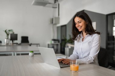 Genç çekici ofis çalışanı gülümsüyor ve bilgisayarında çalışıyor.