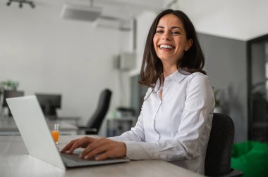 Ofiste dizüstü bilgisayarla çalışan mutlu genç bir kadın..