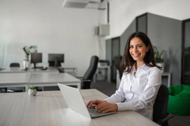 Ofis masasında dizüstü bilgisayarlı gülümseyen kadın çalışan.