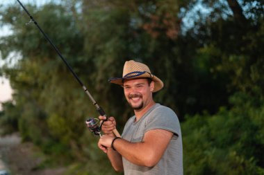 Gün batımında gölde hasır şapkalı neşeli bir balıkçı..