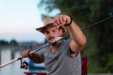 Young angler holding a fishing lure, focus on bait clipart