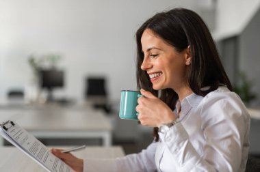 Genç iş kadını ofiste kahve içiyor.