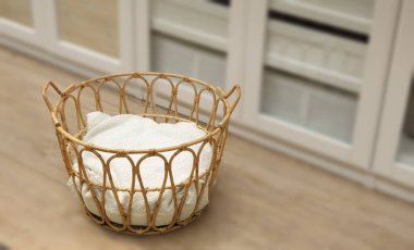 Rattan wicker basket with white natural cushion inside. Selective focus with dressing room decor blurred background. Fashionable storage basket stylish interior item eco design handmade. clipart