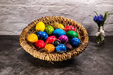 Easter nest with hay and many colorful Easter eggs and a small spring bouquet of flowers