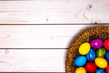 round easter basket with colorful easter eggs on rustic white wooden tabletop