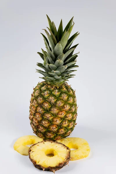 A whole pineapple, with three slices of pineapple in the foreground. Product photo