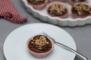 Tabakta çikolatalı cevizli kek servis ediliyor. Pasta tabağı ve arka planda daha fazla muffin ile