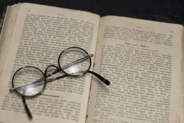 Close-up of an antiquarian book with old German writing and reading glasses with round lenses lying on it clipart