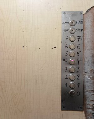 Eski, harap olmuş metal düğmeli asansör kabini.