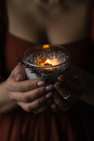 Lavender candle is burning in womans hands. Natural soy wax scented candle withs herbs.High quality photo