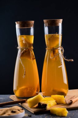 Pineapple Tepache . Refreshing beverage, lightly fermented drink made from fresh pineapple peel and core, plus brown sugar.High quality photo. Served in bottles in low key. Dark background.