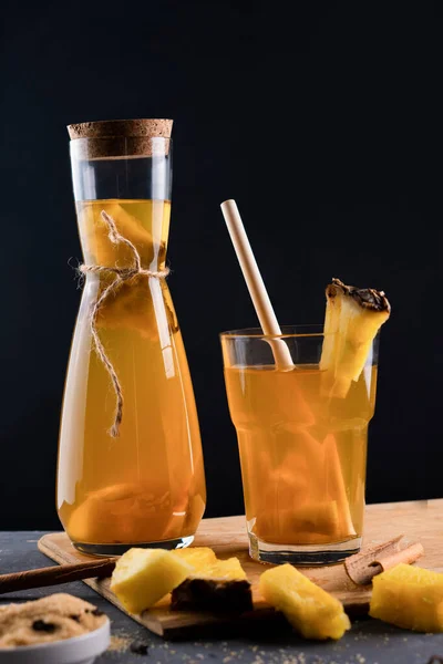 Ananas Tepache. Ferahlatıcı içecek, taze ananas kabuğu ve çekirdekten yapılan hafif mayalanmış içecek, artı kahverengi şeker. Yüksek kalite fotoğraf. Bardakta, şişede sade bir şekilde servis ediliyor. Koyu arkaplan.