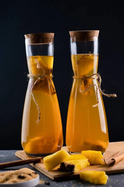 Ananas Tepache. Ferahlatıcı içecek, taze ananas kabuğu ve çekirdekten yapılan hafif mayalanmış içecek, artı kahverengi şeker. Yüksek kalite fotoğraf. Şişe içinde sade bir şekilde servis edilmiş. Koyu arkaplan.