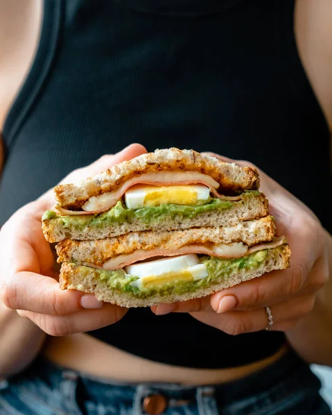 Ellerinde tam tahıllı ekmek, avokado, yumurta, jambon, peynir ve kinoa filizli sağlıklı sandviç tutan kadınlar. Yüksek kalite fotoğraf