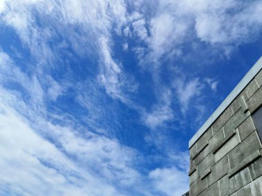 Modern gri beton bir binaya karşı pofuduk beyaz bulutlarla dolu parlak mavi bir gökyüzünün büyüleyici görüntüsü.