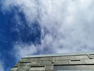 Modern gri beton bir binaya karşı pofuduk beyaz bulutlarla dolu parlak mavi bir gökyüzünün büyüleyici görüntüsü.