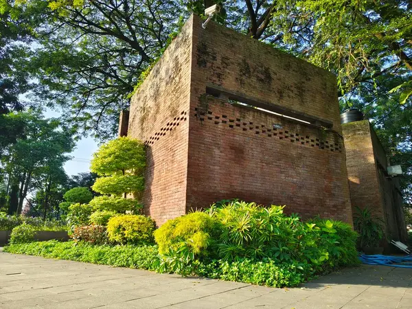 Kediri, Endonezya 3 Haziran 2023 - Yazın yeşil ağaçlar ve doğal kırmızı tuğla binalar olan gölgeli bir park, dinlenme yeri