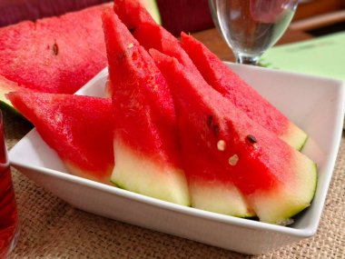 Beyaz bir porselen tabakta karpuz dilimleri ve sağlıklı bir vücut için bir bardak su, beyaz tabakta karpuz dilimleri.