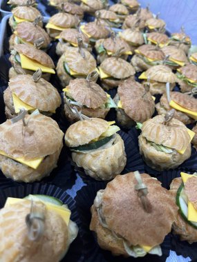 Elegant bite-sized choux sandwiches with cucumber, cheese, and lettuce, served in black cups, perfect for stylish catering events