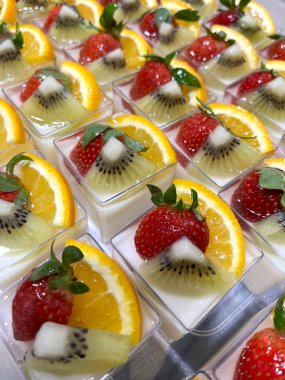 Fincanda taze meyve panna cotta, üzerine çilek, kivi ve portakal dilimleri, renkli ve ferahlatıcı bir tatlı için..