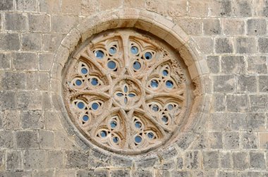 Kıbrıs Rum Kesimi, Kyrenia 'daki Bellapais Abbey' den izole edilmiş bir daire penceresi fotoğrafı. Pencere sarı ve kahverengi duvarlar arasında ve içinde cam var. Pencere çiçek şekli gibi..