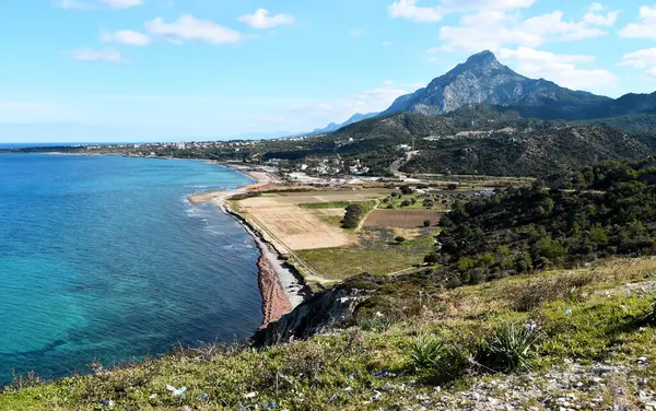Karsiyaka / Vasilia Kıbrıs 'taki manzara fotoğrafı. Mavi deniz, yeşil kahverengi toprak ve arkadaki dağda bulutlu mavi gökyüzü görülür..